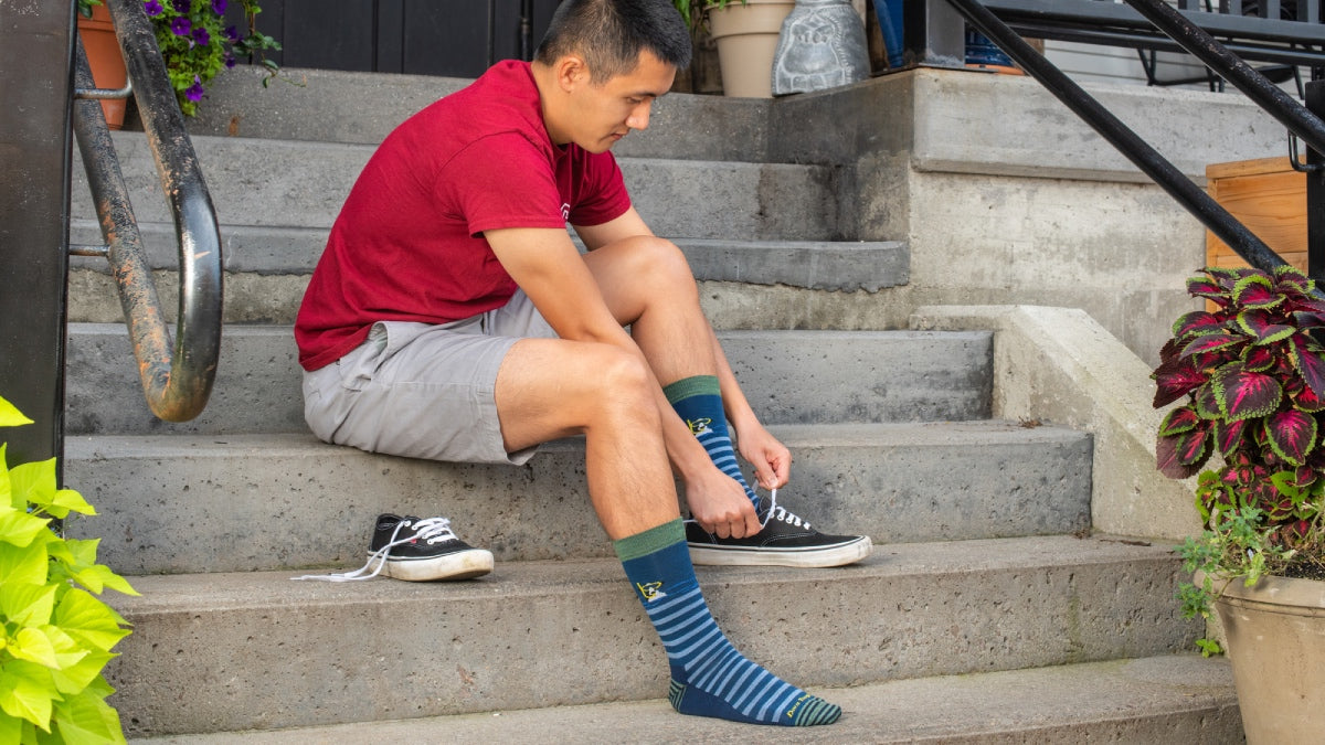 Man seated on steps putting on converse and merino wool socks for walking