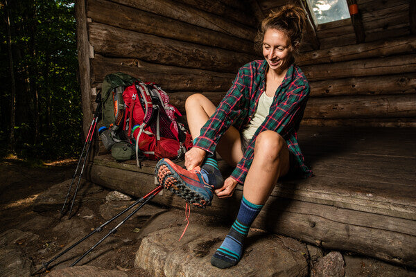 Hiker pulling on hiking boots over midweight merino wool socks for a summer hike