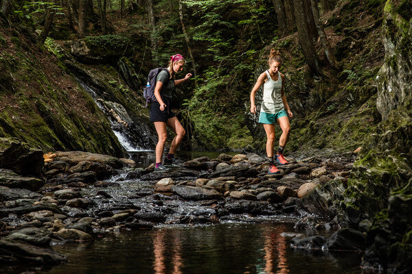 Two hikers crossing a stream wearing merino wool hiking socks