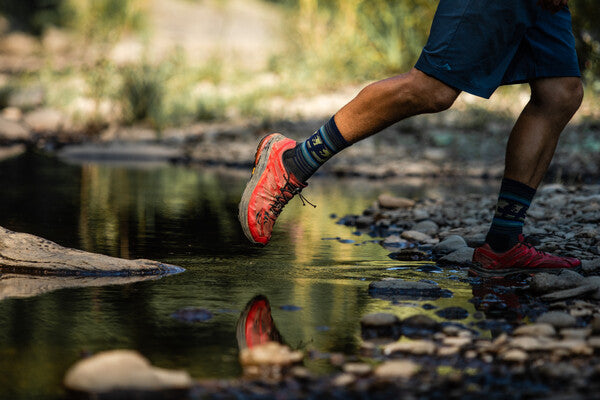 Hiker crossing stream wearing moisture wicking darn tough hiking socks with trail shoes