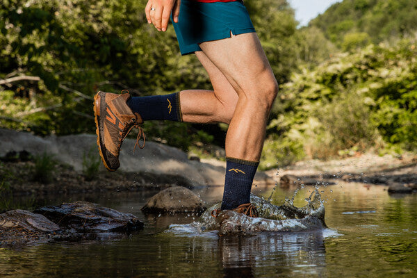 Hiker walking through a stream wearing the men's hiker boot socks in deep blue