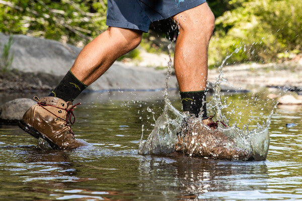 Hiker walking through river wearing merino wool boot socks and hiking boots