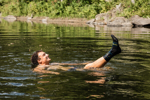 Hiker taking a swim in a mountain stream, foot poking out of water wearing darn tough socks