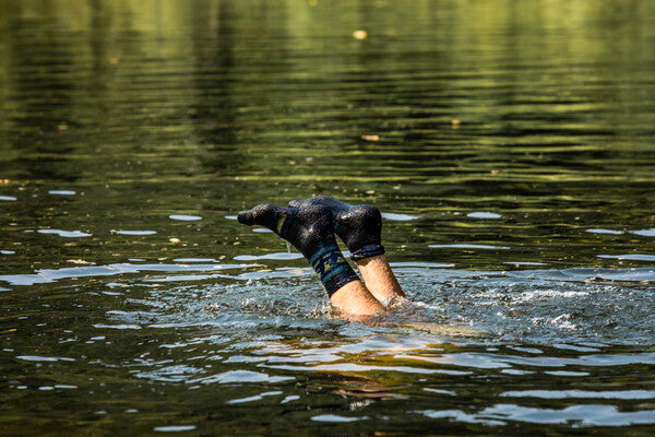 Person diving into a lake, with their merino wool sock clad feet just sticking up