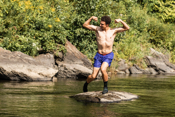 Hiker standing in middle of lake wearing wet socks and flexing his muscles after a good swim