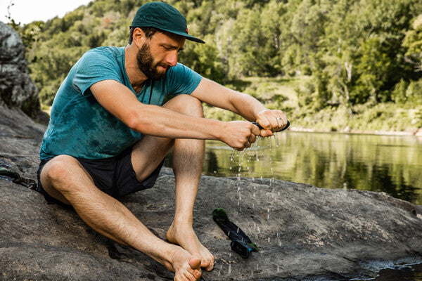 Hiker seated by stream wringing water out of his socks to help them dry faster