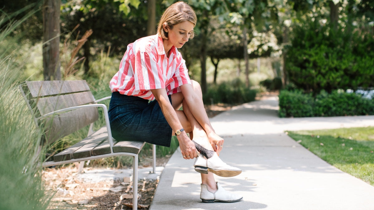 Woman seated on park bench adjusting shoes and wearing darn tough socks, a great Mother's Day gift