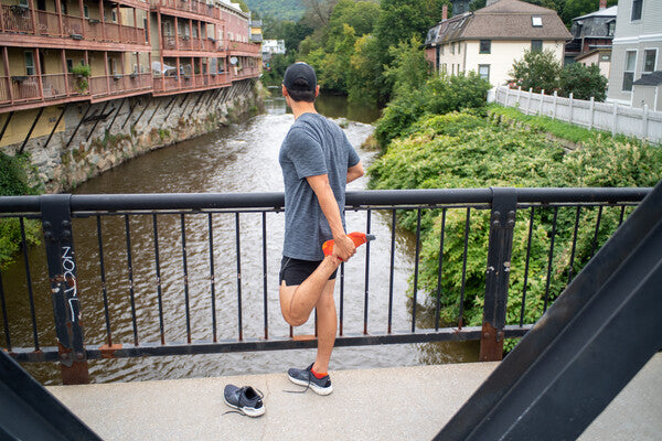 Runner paused on a bridge to stretch, wearing orange merino run socks