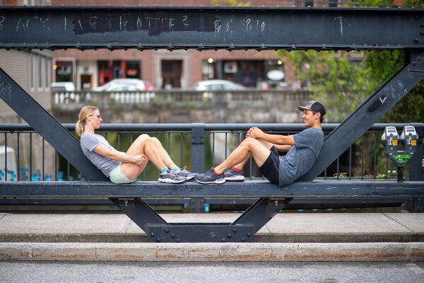 Man and woman runner seated on bridge wearing no show socks, taking a break