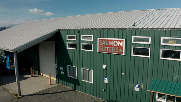 A large green building in Alaska with a sign that says "Salmon Sisters"