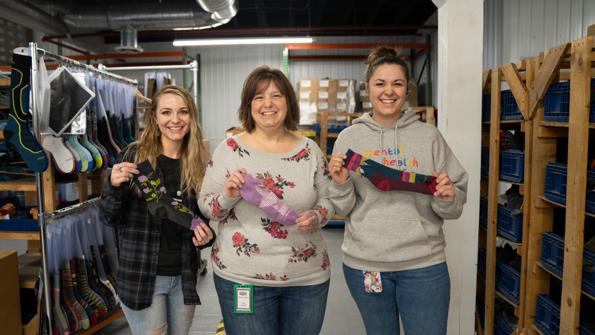 Two daughters standing with their mom, showing what socks they'd buy her for mother's day