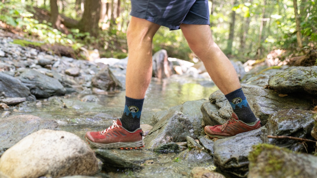 Hiker crossing a stream wearing long lasting socks from Darn Tough Vermont