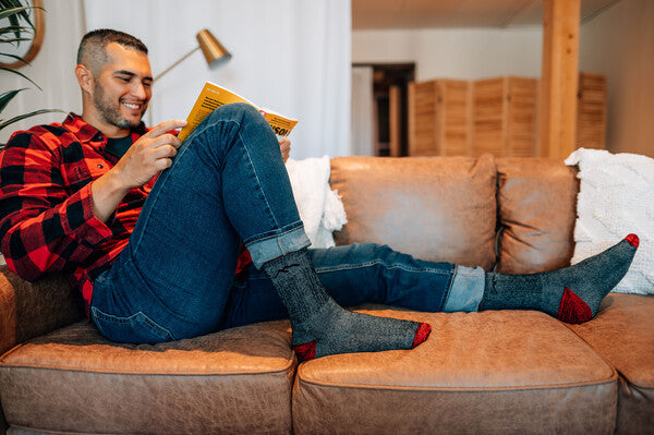 Man with large feet reading on a couch wearing heavyweight darn tough socks