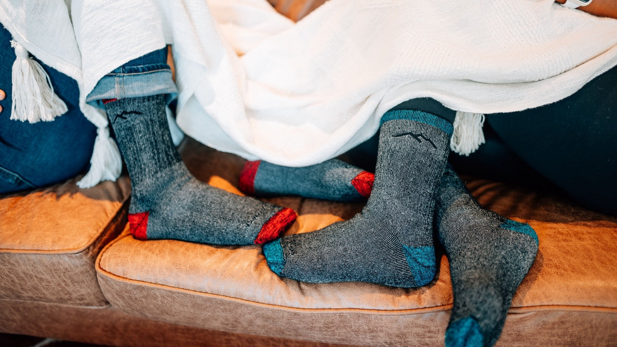Two pairs of feet sticking out from under a blanket, wearing super soft merino wool socks, no itch