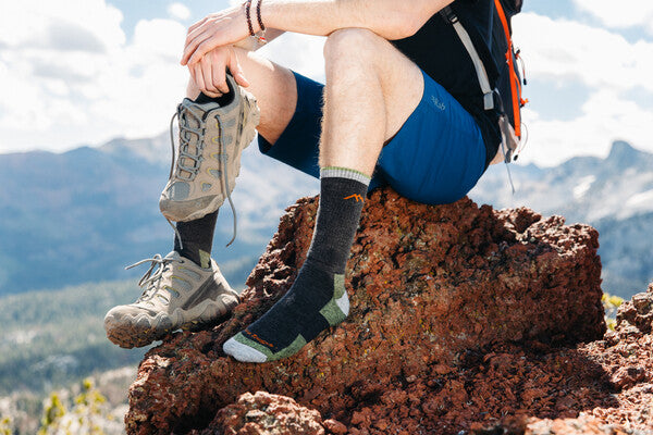Hiker seated on rock with one hiking shoe off, showing their darn tough socks