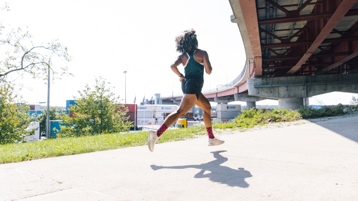 Woman starting her run, headed out in pink socks as she passes under a bridge