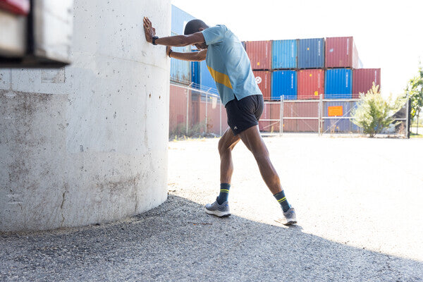 Runner doing a stretch against a wall to care of himself