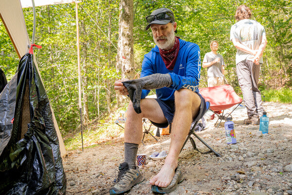 A thru hiker with one sock off, examining it