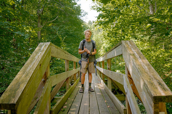Thru hiker "Smores" standing on a bridge wearing sandals and darn tough socks