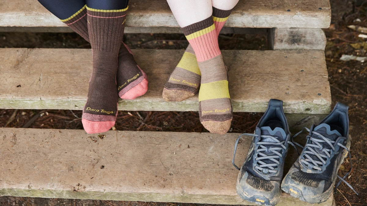 Two pairs of feet wearing merino wool hiking socks in brown and pink