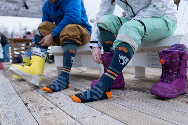 A skier and a snowboarder each wearing the High Fives ski socks