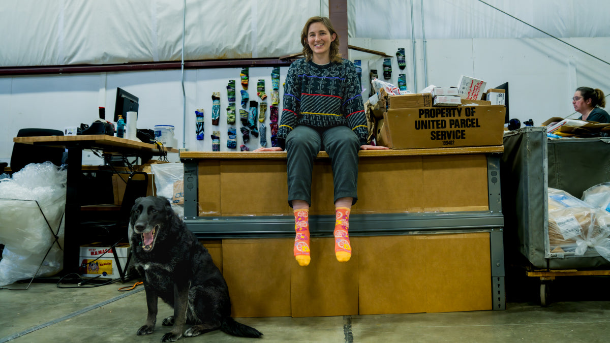 Emily sitting on her desk wearing her favorite socks with her dog nearby