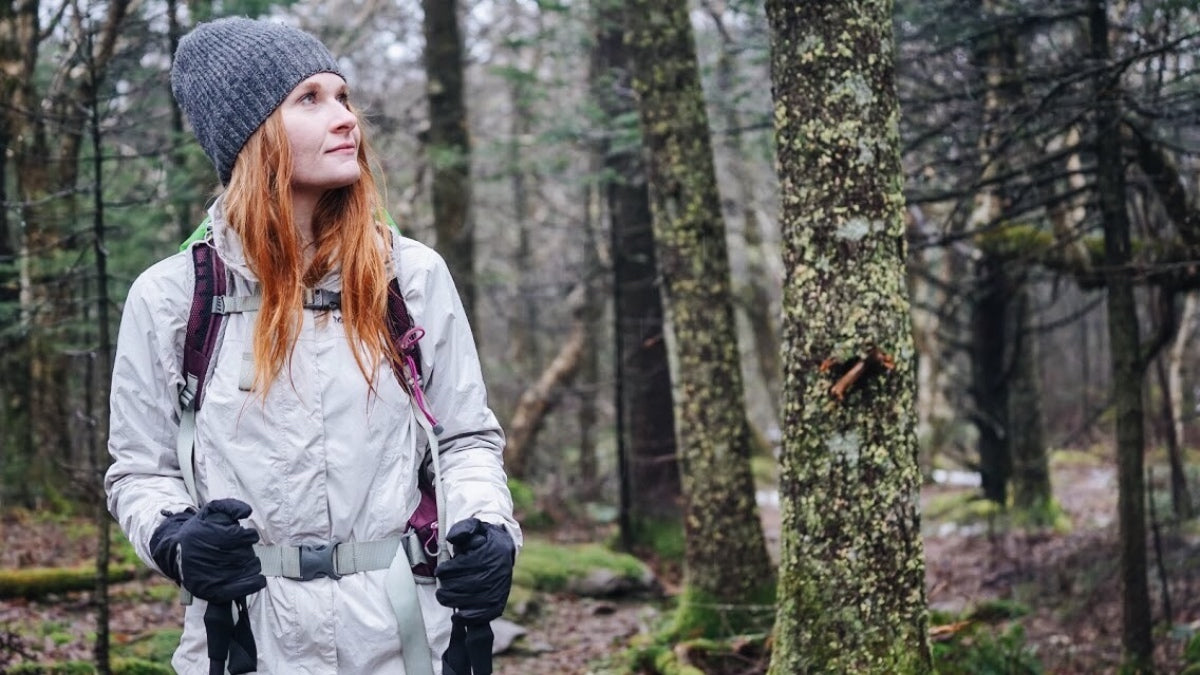 Woman out in the woods wearing a raincoat, hat, gloves and other examples of what to wear hiking