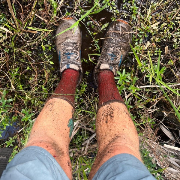 A pair of very dirty feet wearing sneakers and darn tough socks