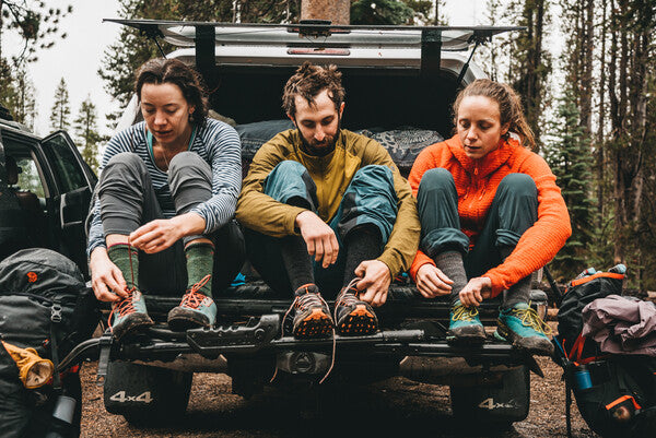 Three hikers on a tailgate getting their hiking shoes and socks off