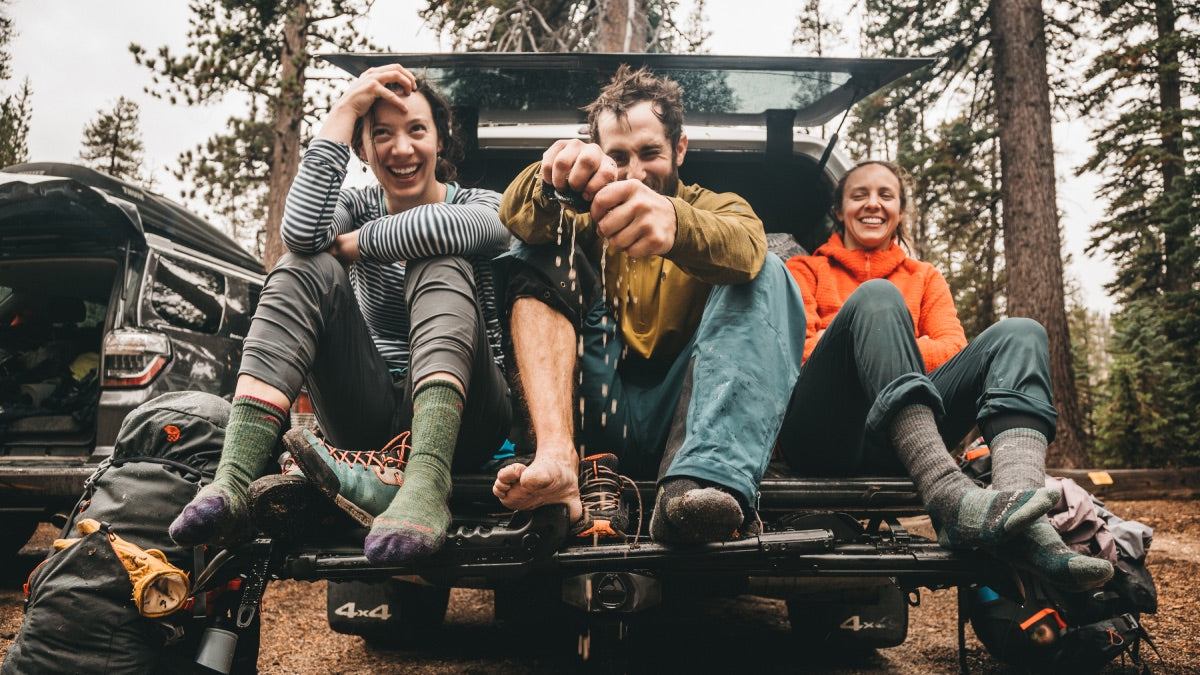 Three hikers on rainy day wearing moisture wicking socks, seated on tailgate drying off