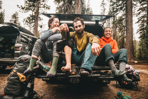 Group of hikers seated on tailgate drying off their socks after a long day