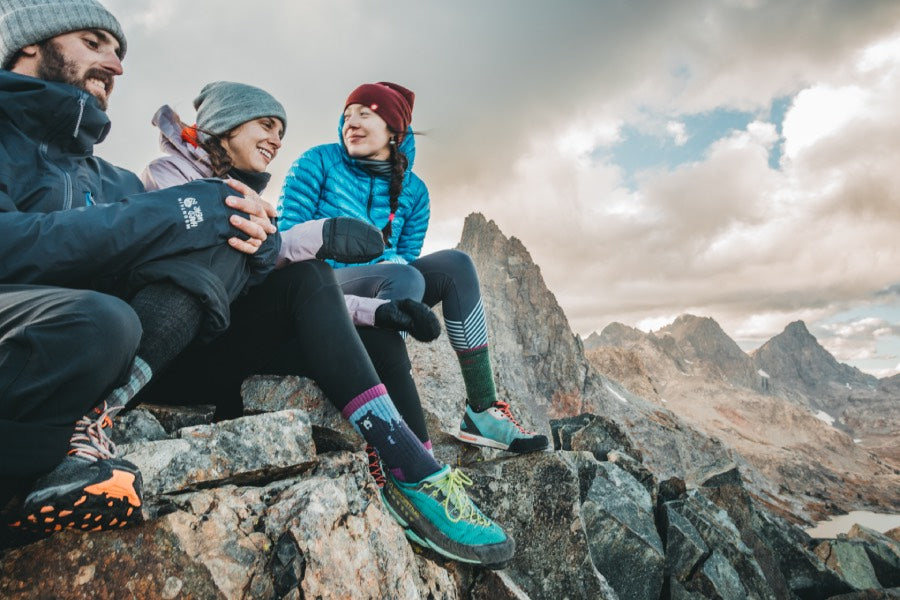 Three hikers seated on summit taking in view wearing darn tough hiking socks