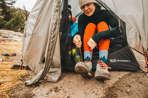 Woman leaning out of tent to pull on shoes over Treeline hiking socks