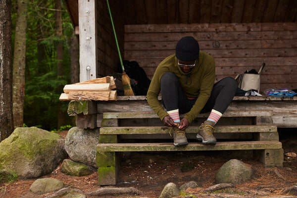 Hiker seated in shelter tying shoelaces and wearing the Gatewood boot hiking sock