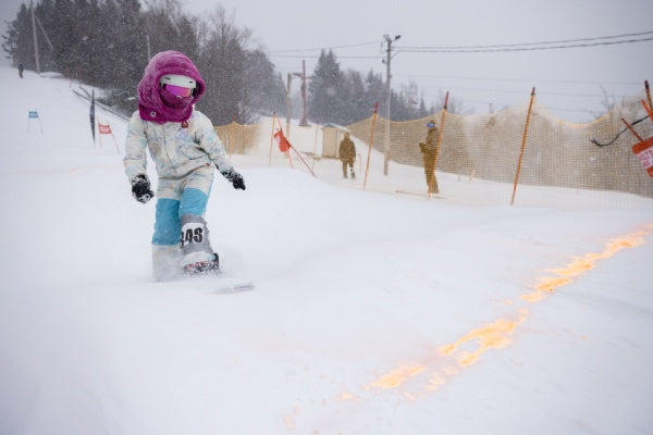 A young girl snowboarder about to cross the finish line