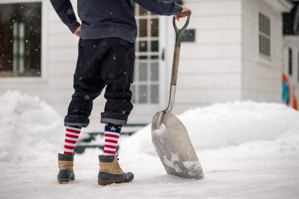 Man shoveling snow in boots and Darn Tough Captain Stripe Over-the-Calf Socks