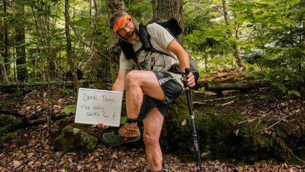Thru hiker showing off his Darn Tough socks with a sign saying "The only socks for the AT"