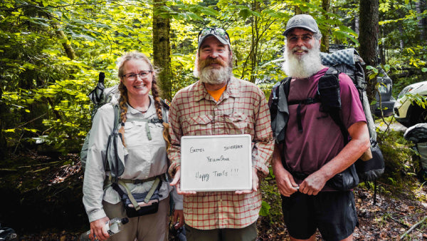 Three thru hikers with a sign saying "happy trails"