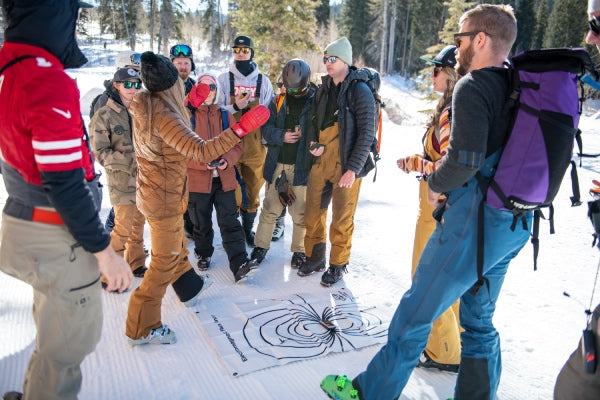 Clinic participants in a circle listening to the instructor explain a snow safety concept