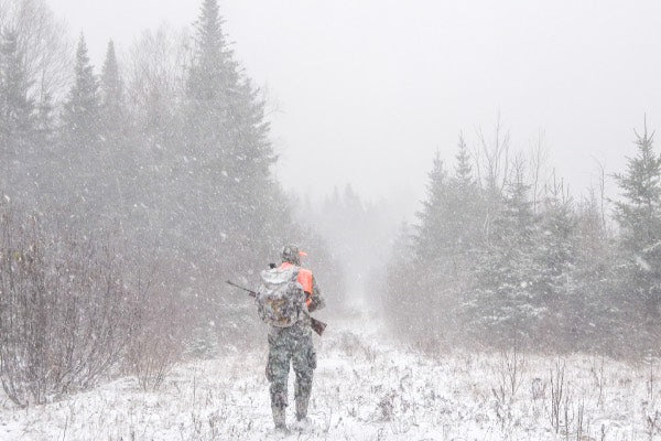 Hunter getting snowed on while tracking a deer through a snow storm