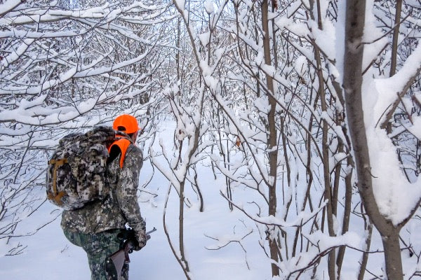 Hunter in camo walking through woods in deep snow