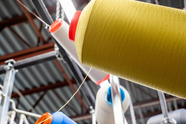 A cone of yellow Merino Wool yarn, with a thin thread going out toward the knitting machine