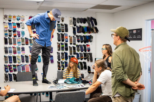 Jake Blauvelt standing on a table surrounded by Darn Tough designers, wearing sock prototypes