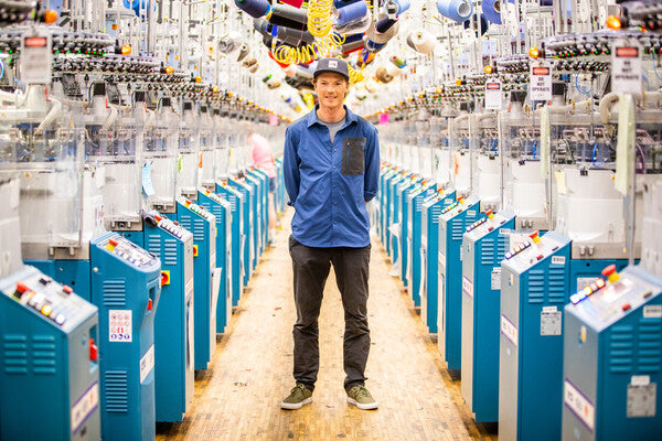 Jake Blauvelt standing in the rows of knitting machines at the Mill