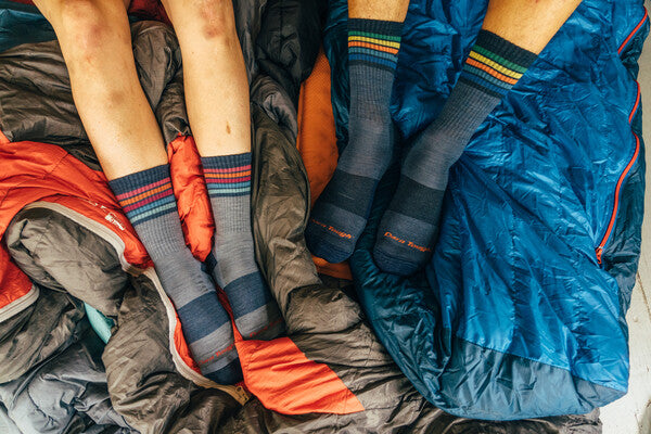 Two pairs of feet on sleeping bags wearing the men's and women's Kelso hiking socks