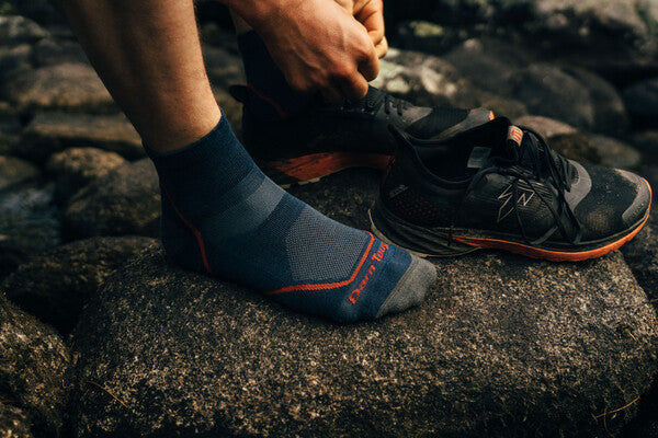 Hiker putting on shoes and merino wool all weather performance socks from Darn Tough