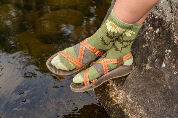Feet hanging down wearing sandals with green socks with a white daisy pattern