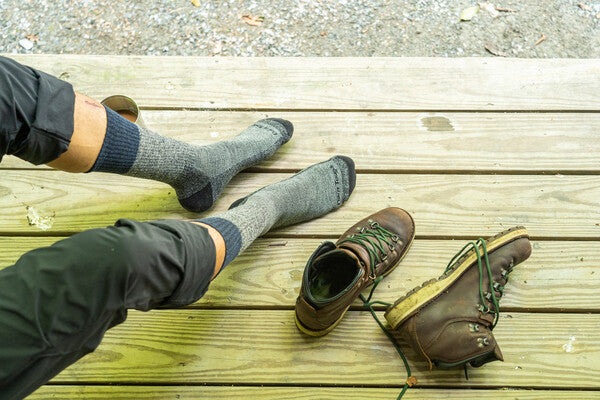 Person seated on deck with boots off, wearing gray boot socks