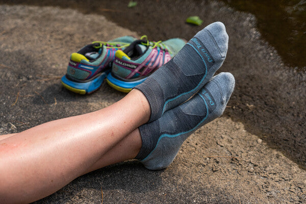 Hiker seated on rock with shoes kicked off showing their no show hiking socks from darn tough