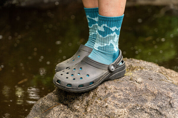 Feet wearing blue darn tough socks with gray crocs